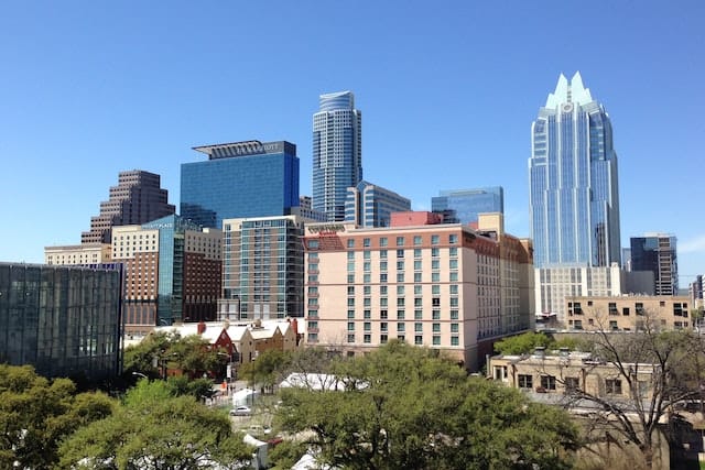 Austin skyline with modern skyscrapers, trees in foreground under clear blue sky