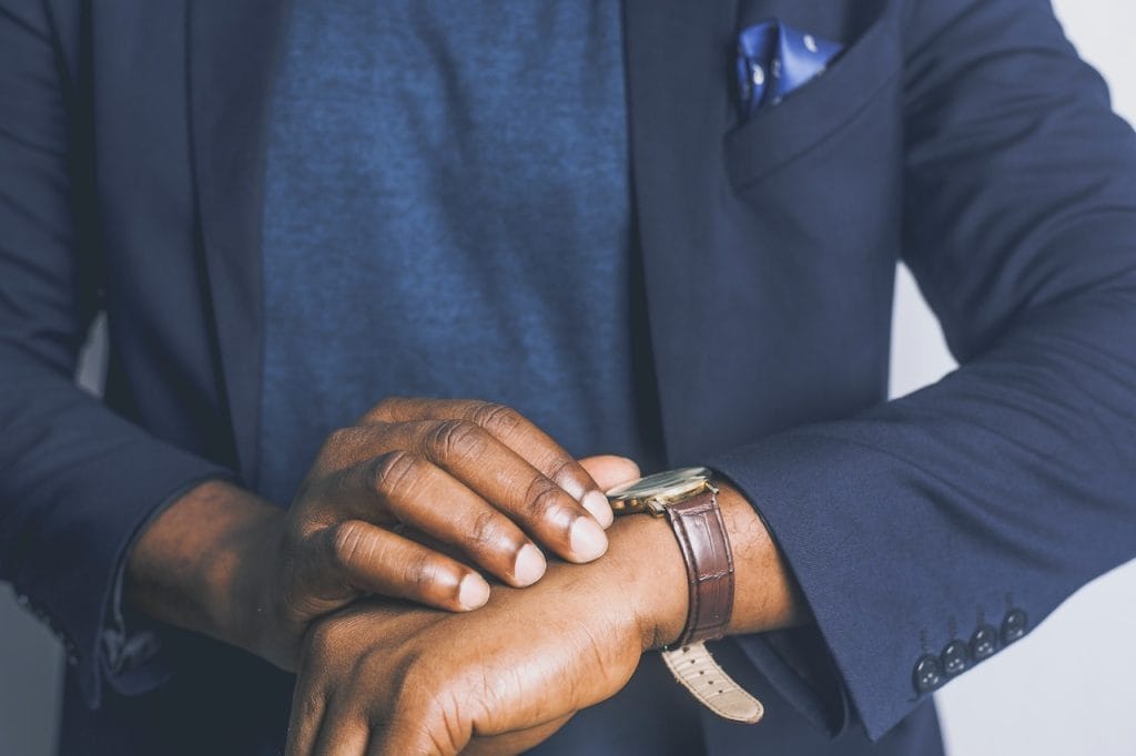 Man in navy blazer checking watch, wearing blue shirt and pocket square