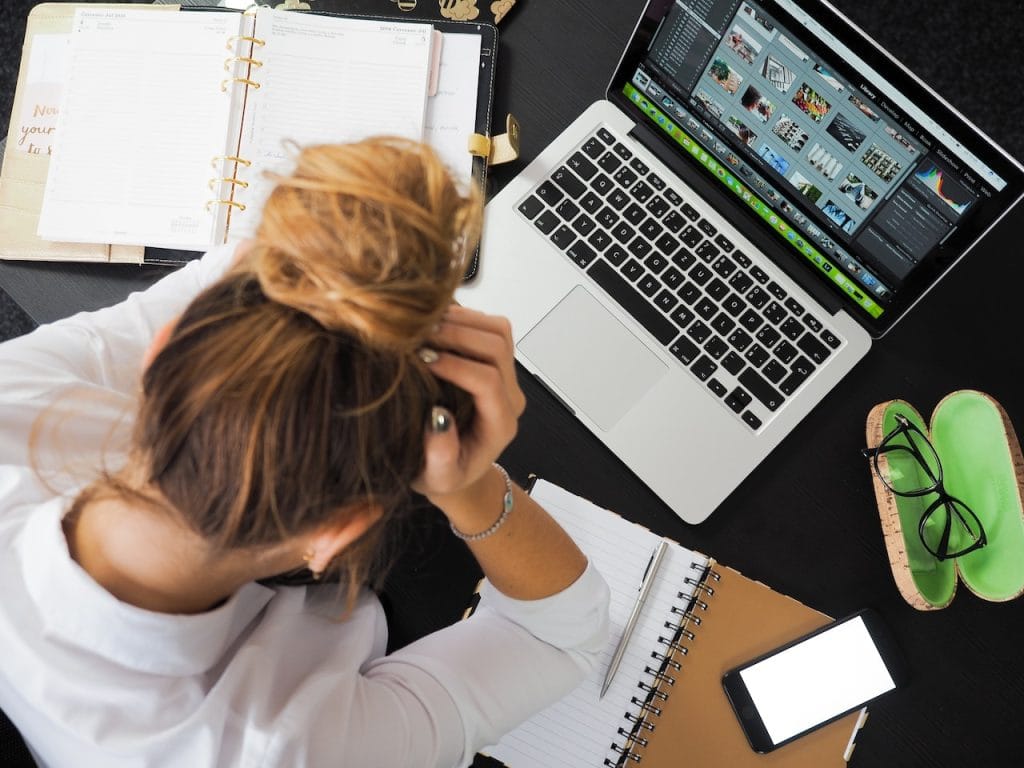 Stressed woman at desk with laptop, planner, and phone, holding head