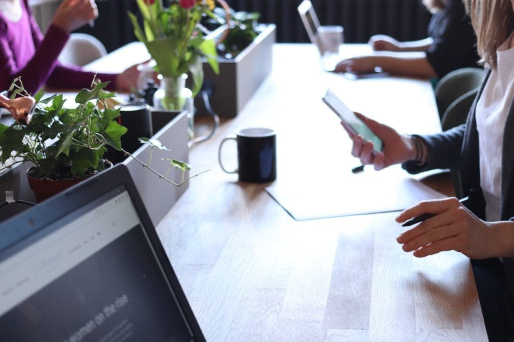 People working at table with laptops, phones, and plants in relaxed office