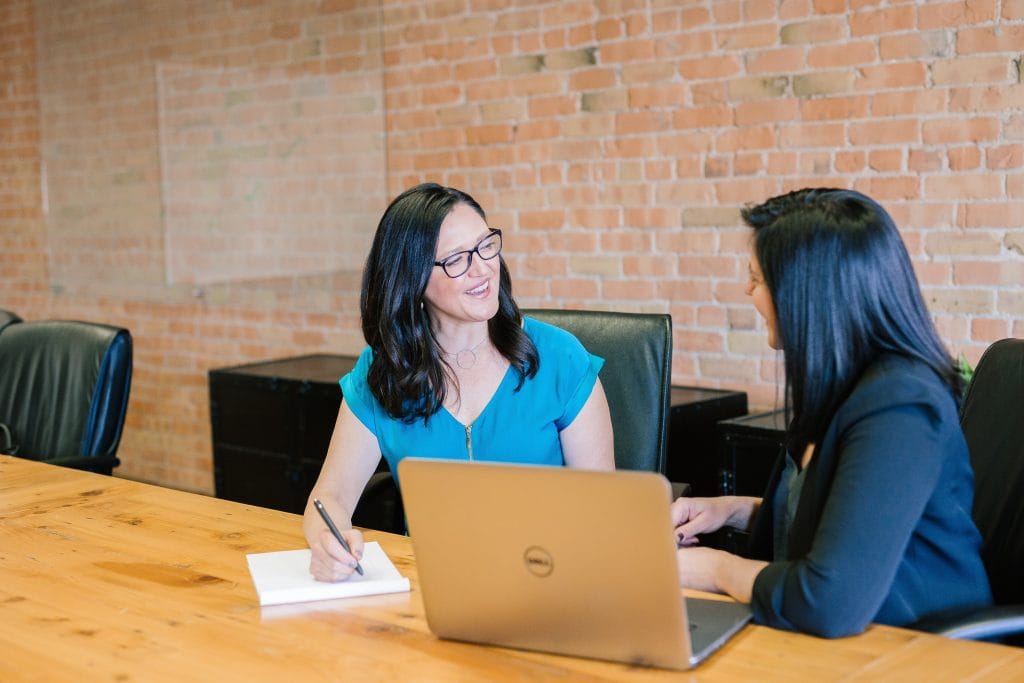 Two women smiling and discussing work over laptop in meeting room