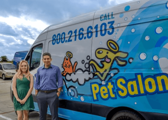 Two people smiling beside colorful pet salon van outdoors