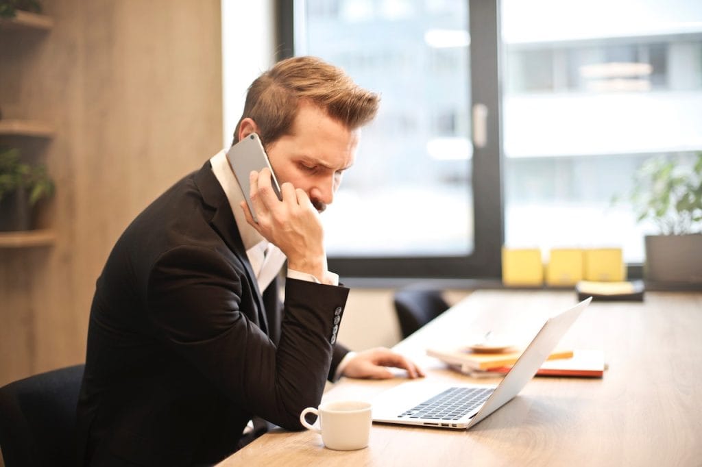Businessman on phone working at laptop in bright office