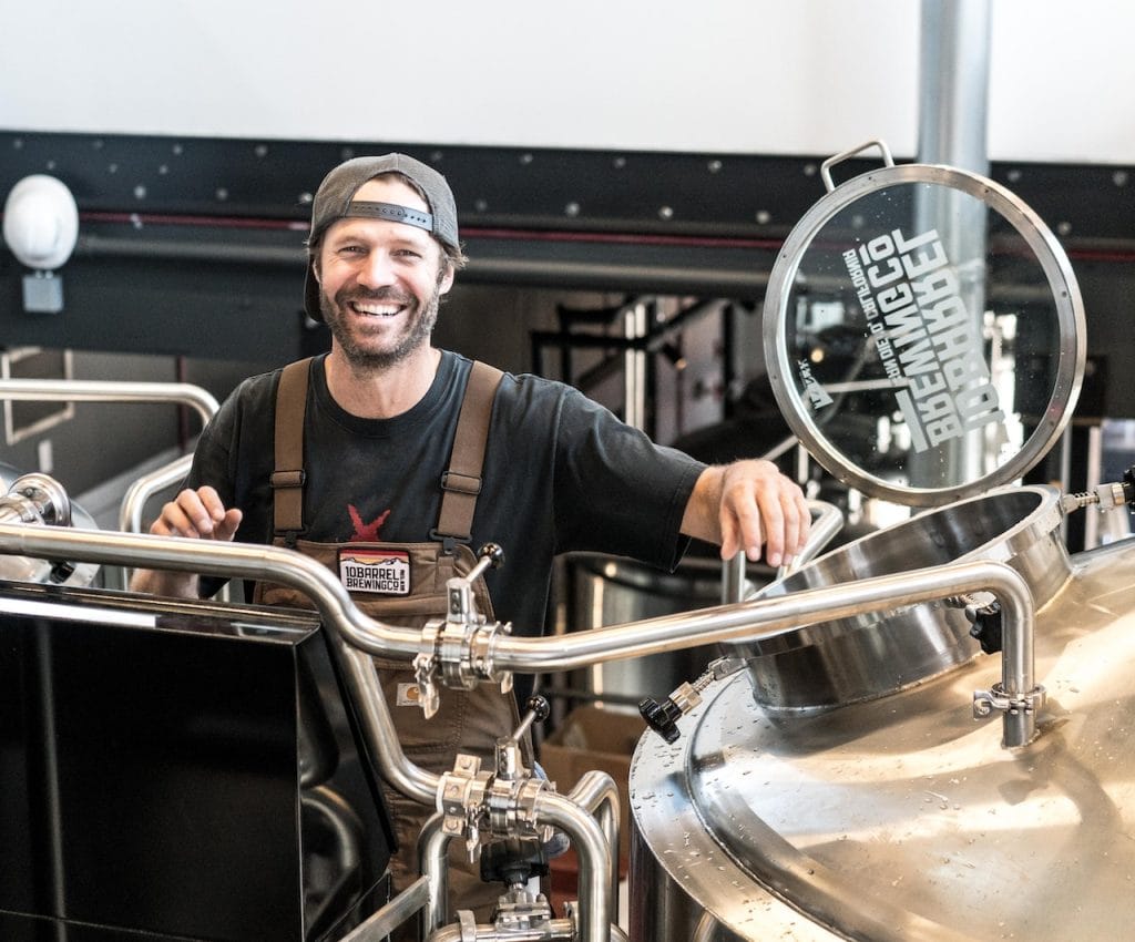 Man in brewery standing beside large steel vessel