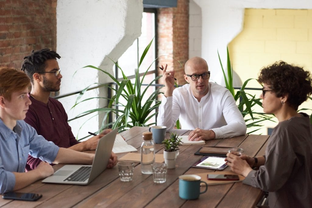 Team meeting around table with laptops, notes, and drinks