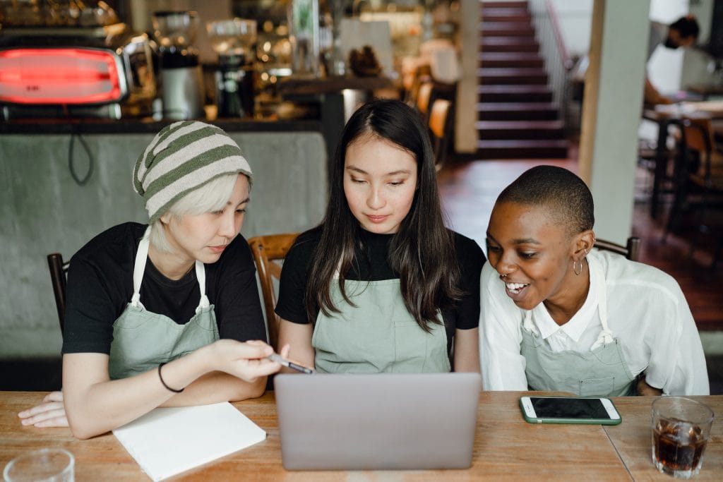 Three café workers discussing over laptop wearing aprons