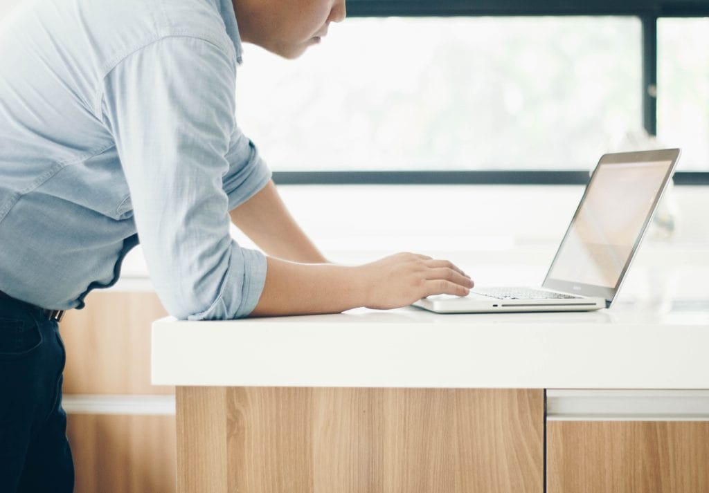 Person leaning over laptop on kitchen counter