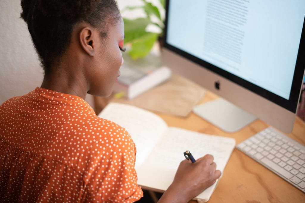 Woman writing notes while looking at computer