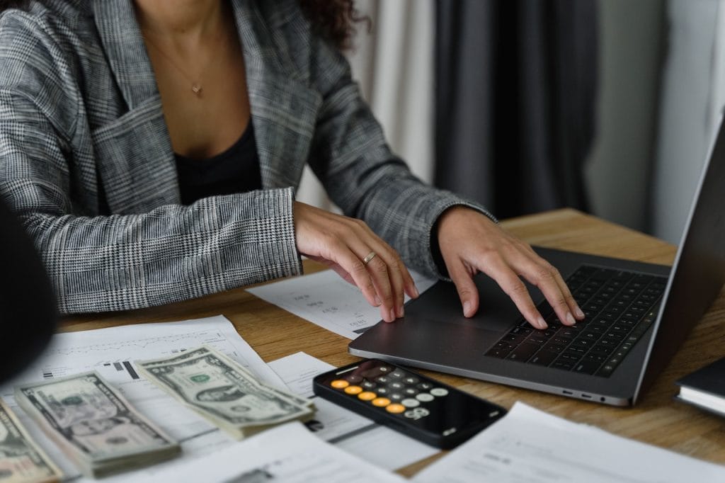 Person using laptop with money and calculator on desk